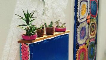 Una puerta azul adornada con un tapiz de ganchillo colorido, una repisa con plantas en macetas y una pared con textura.