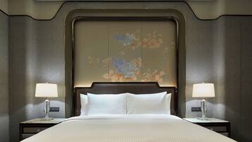 Una cama grande con sábanas blancas, flanqueada por dos mesitas de noche con lámparas, en una habitación con un cabecero decorativo y un mural floral.