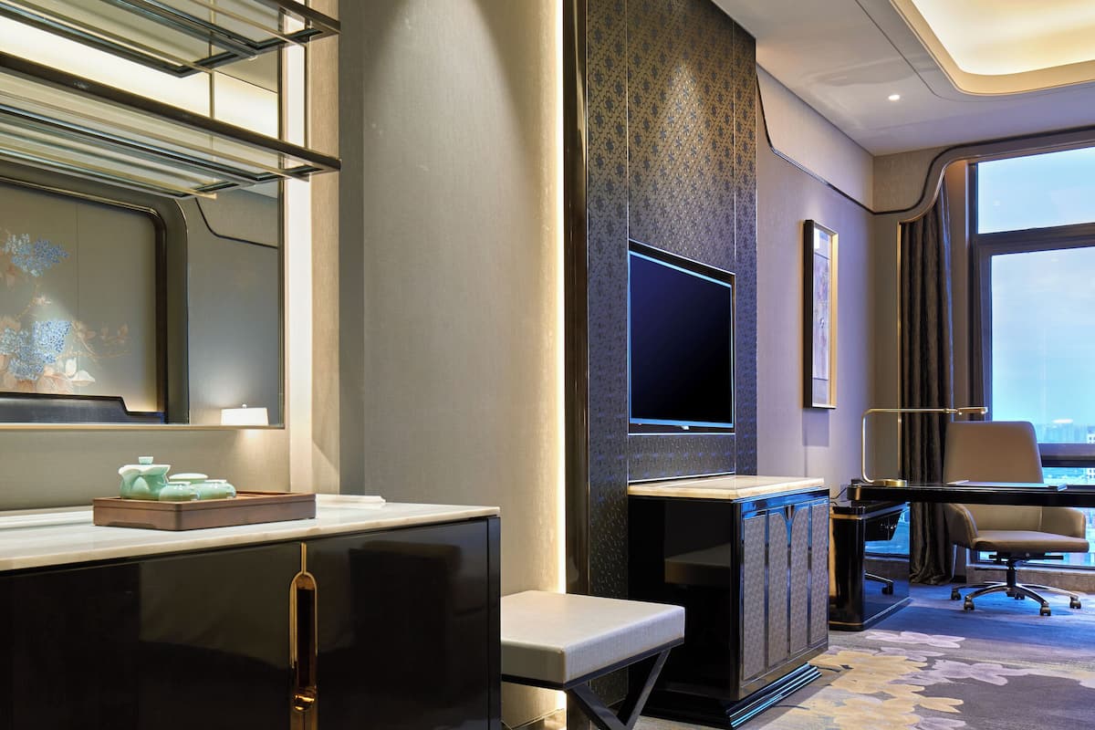 A modern hotel room with a large flat-screen TV, a desk, and a comfortable seating area.