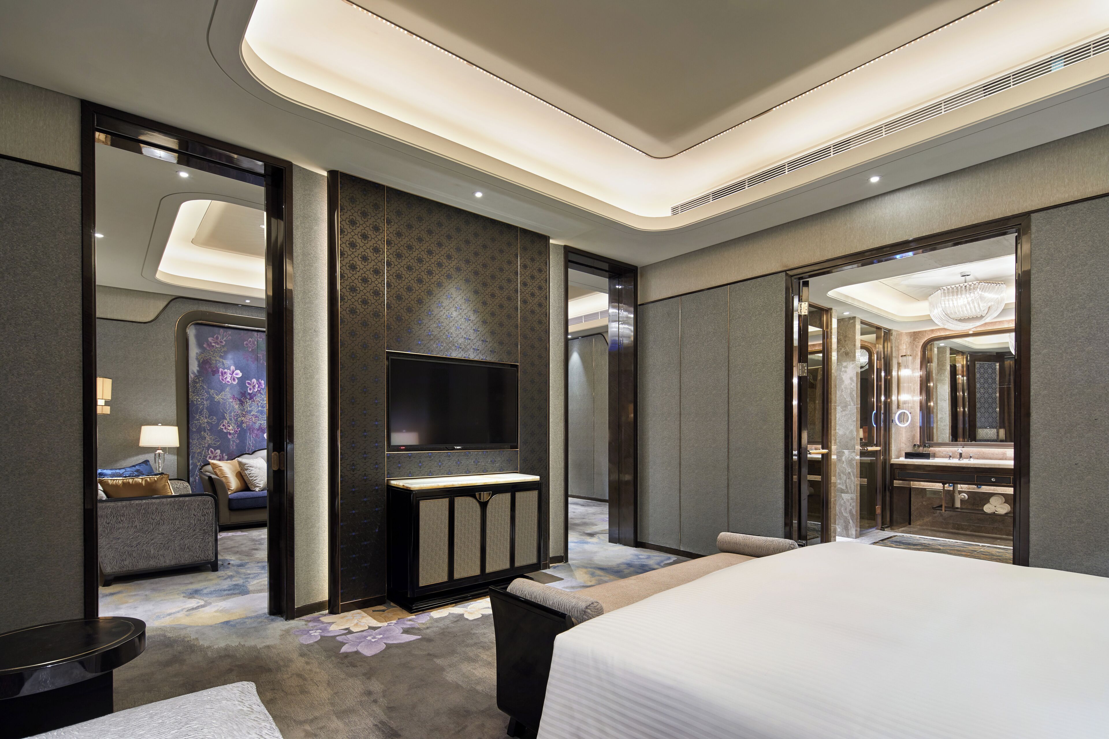 A modern hotel room with a large bed, a flat-screen TV, a vanity with a mirror, and a seating area with a sofa and a small table.