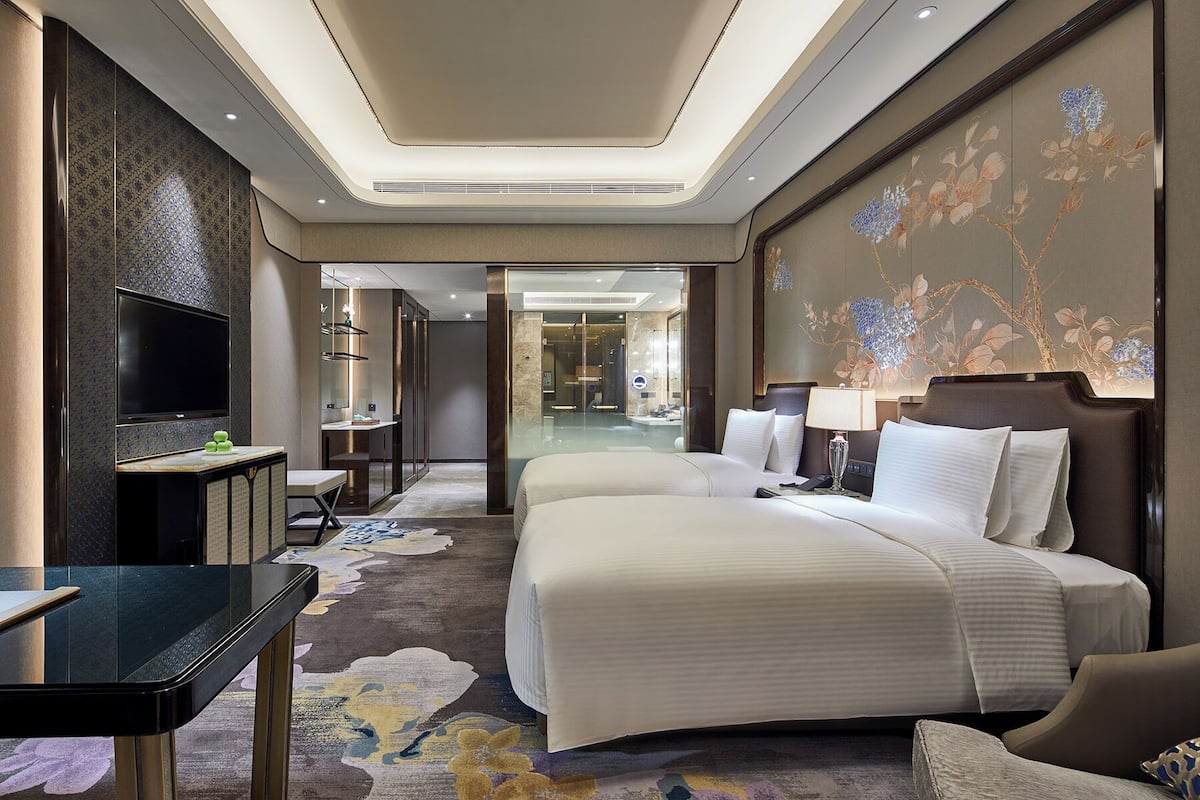 A hotel room with a large bed, a TV, a desk, and a bathroom visible through an open door.