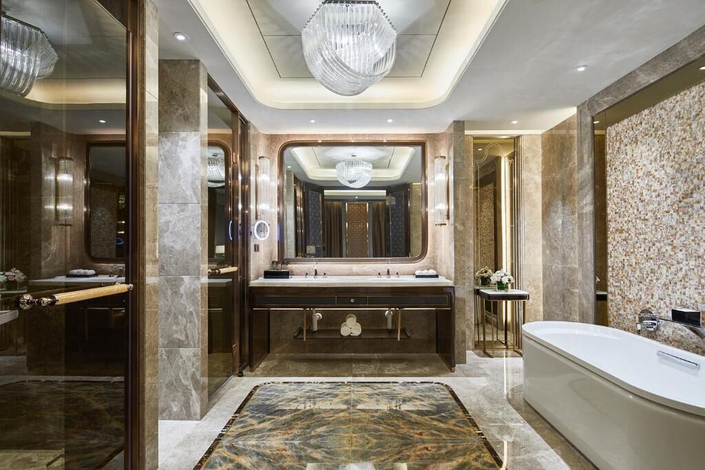 A luxurious bathroom with a large mirror, a freestanding bathtub, and a marble floor.