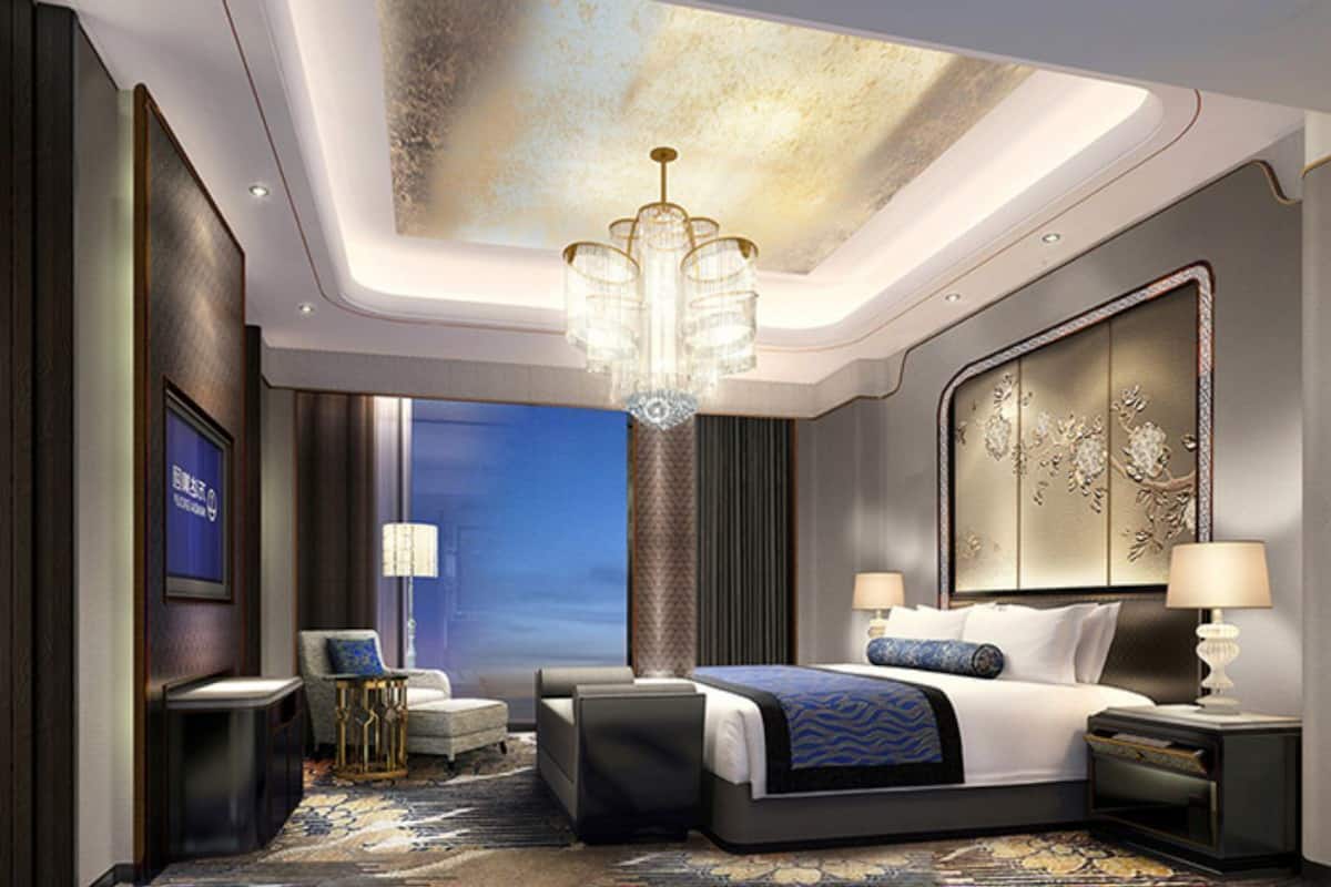 A modern hotel room with a large bed, a chandelier, a view of the city, and a large artwork on the wall.