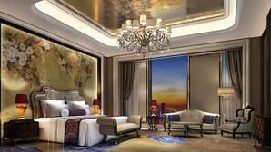 Ein luxuriöses Schlafzimmer mit einem großen Bett, einer Sitzecke und Blick auf eine Stadtlandschaft im Abendrot.