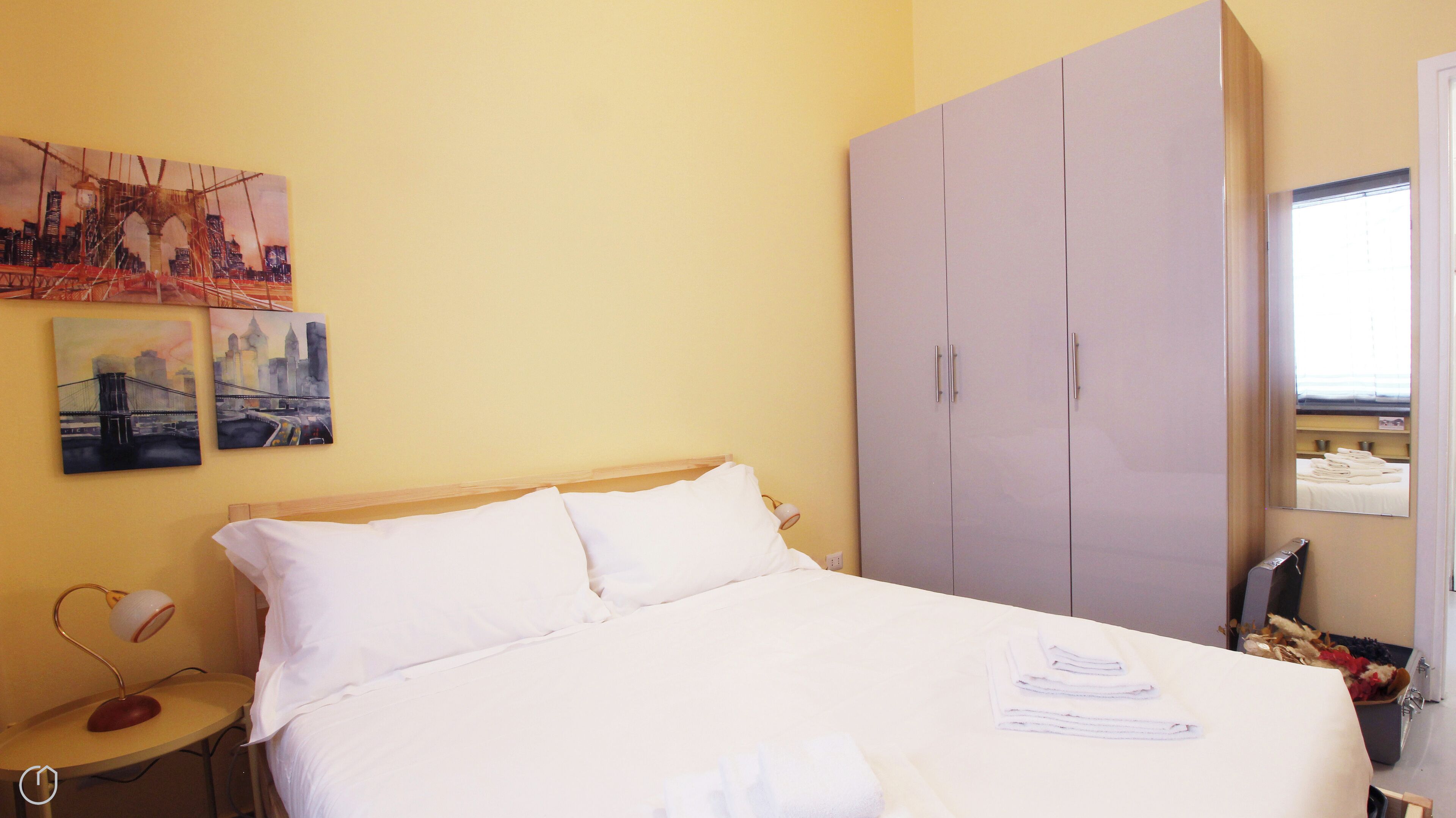Una habitación de hotel con cama, armario, mesita de noche y dos cuadros en la pared.