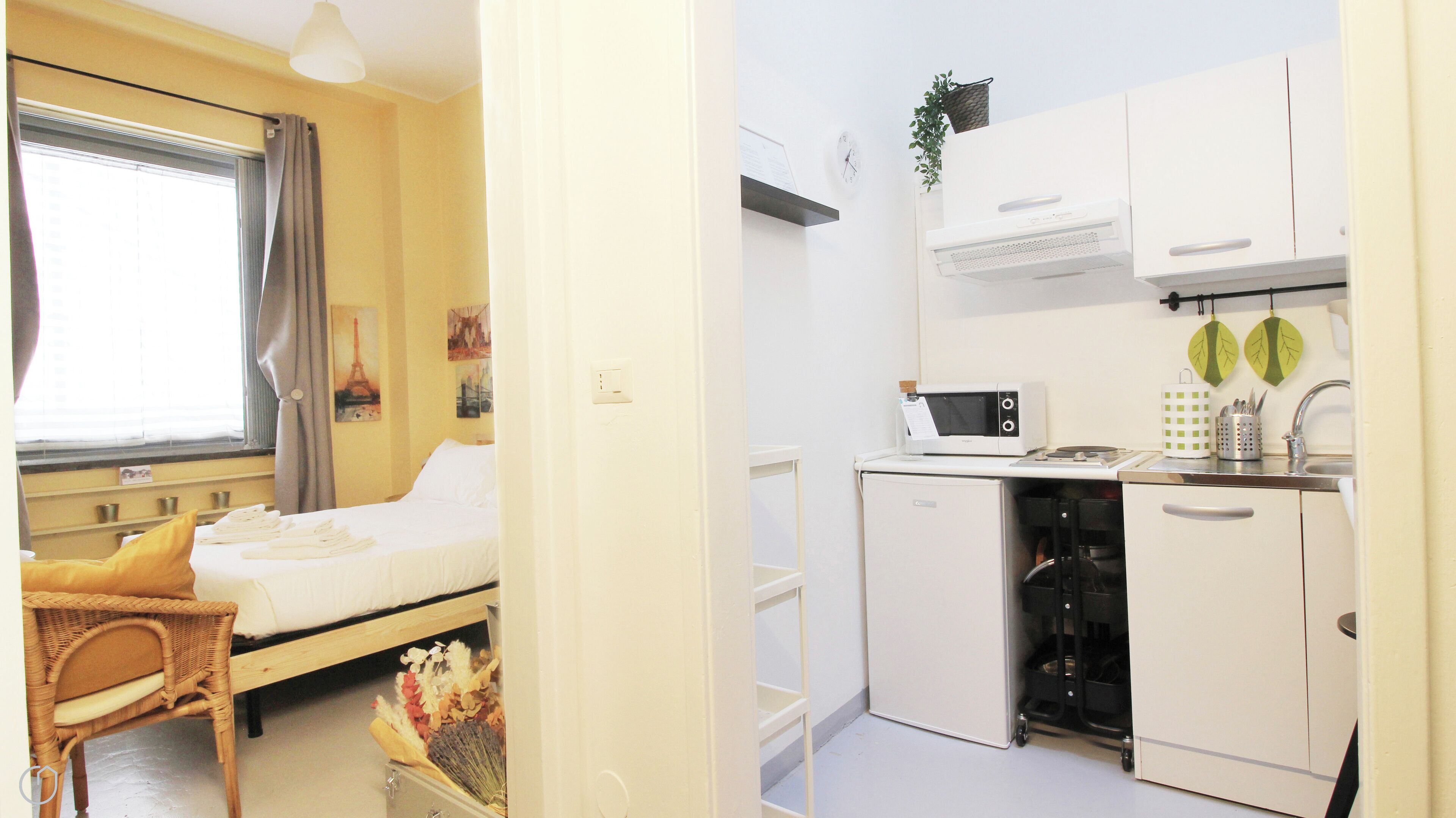 A compact room with a bed, a small dining table, a kitchenette with a microwave, and a sink.