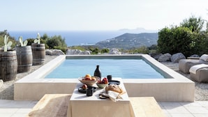 Un patio con una mesa lista para una comida, con vista a una piscina y un paisaje pintoresco.