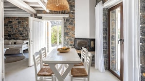 Un comedor con mesa y sillas blancas, una lámpara colgante de mimbre, una pared de piedra y una chimenea.