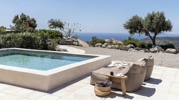 A pool area with a view of the sea, outdoor seating, and a stone pathway.