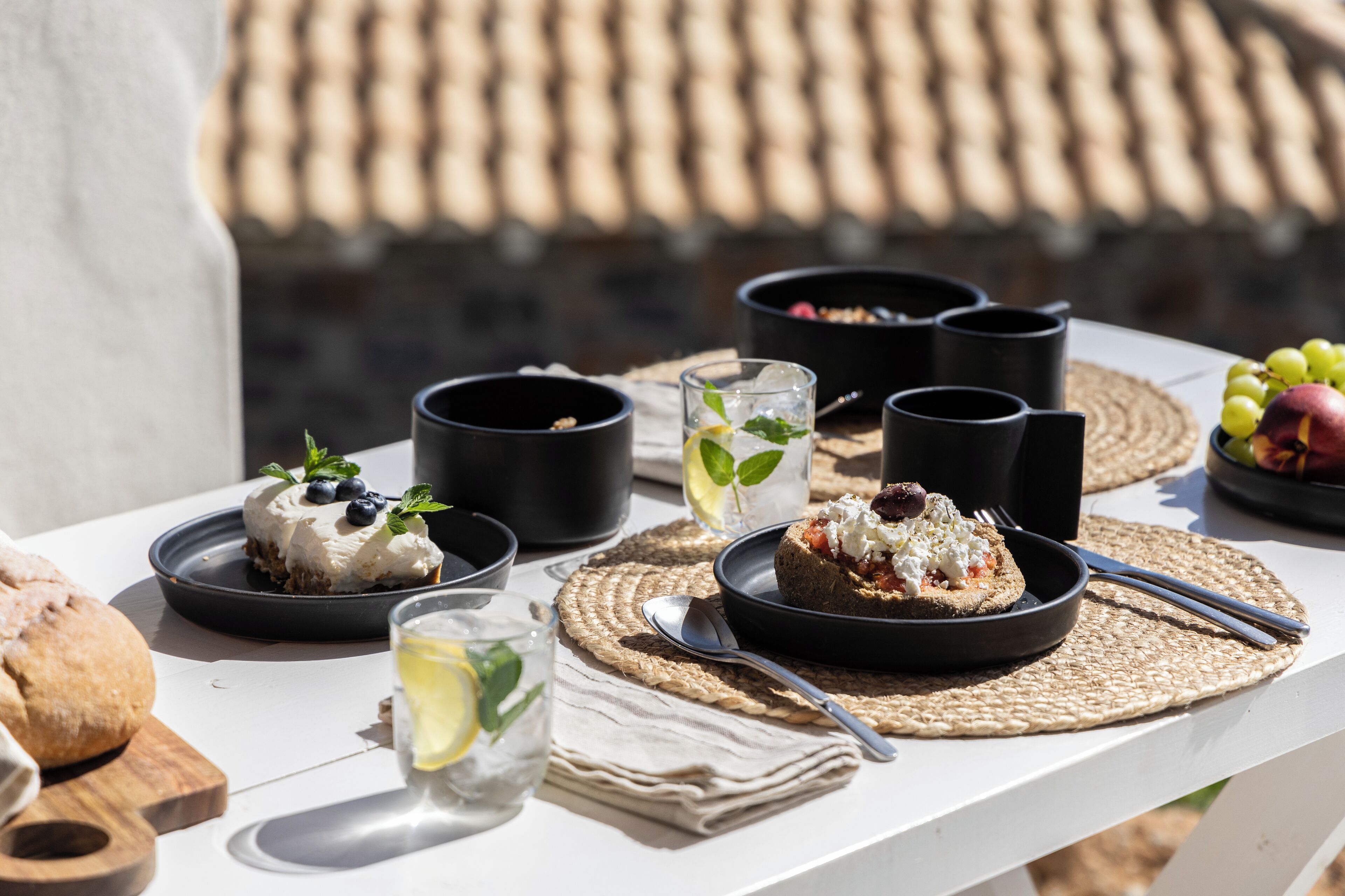 Una mesa dispuesta con comida y bebidas, incluyendo platos de comida, vasos y tazas negras.