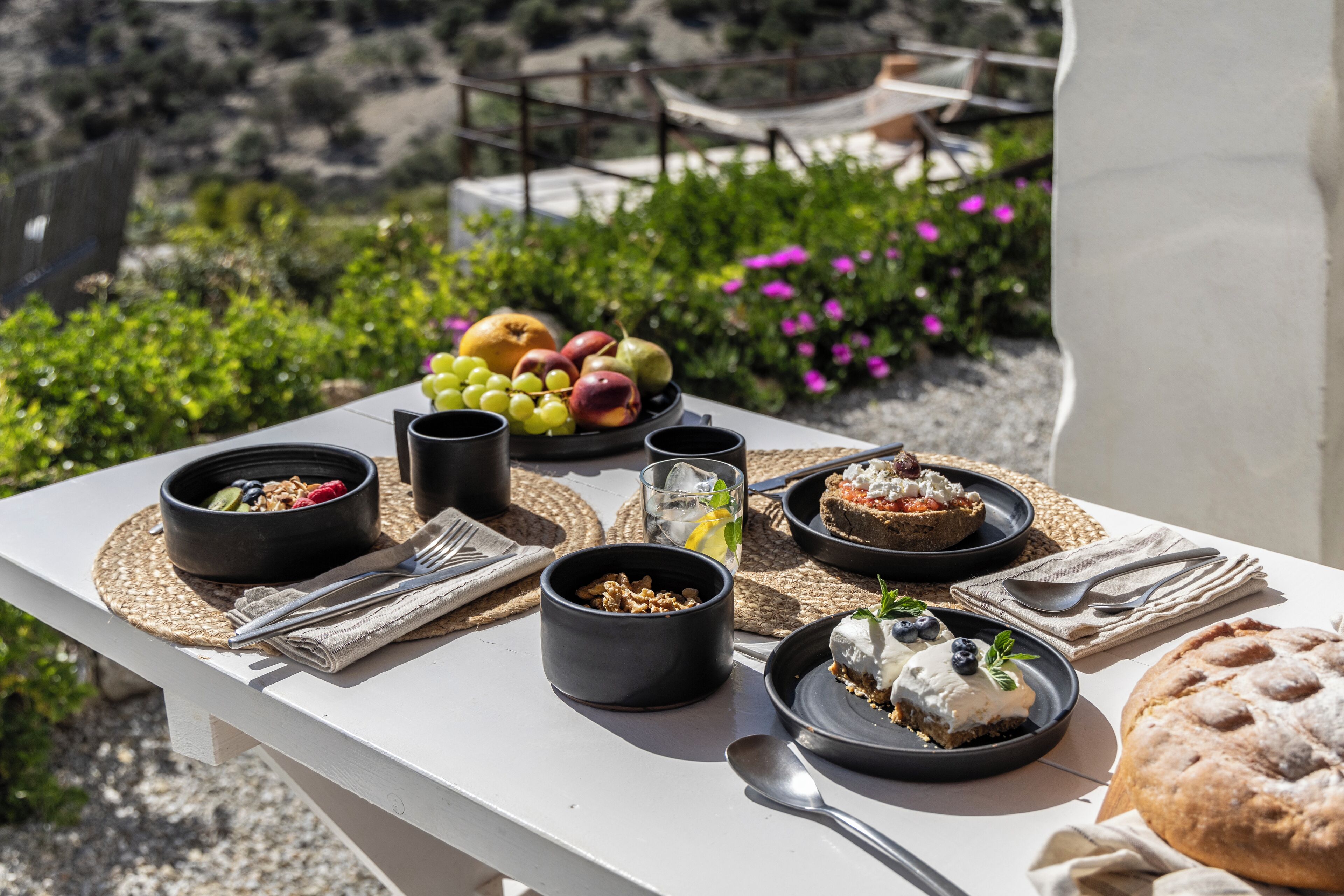 Una mesa dispuesta con alimentos para el desayuno, como frutas, pan y bebidas, con una vista panorámica al exterior.