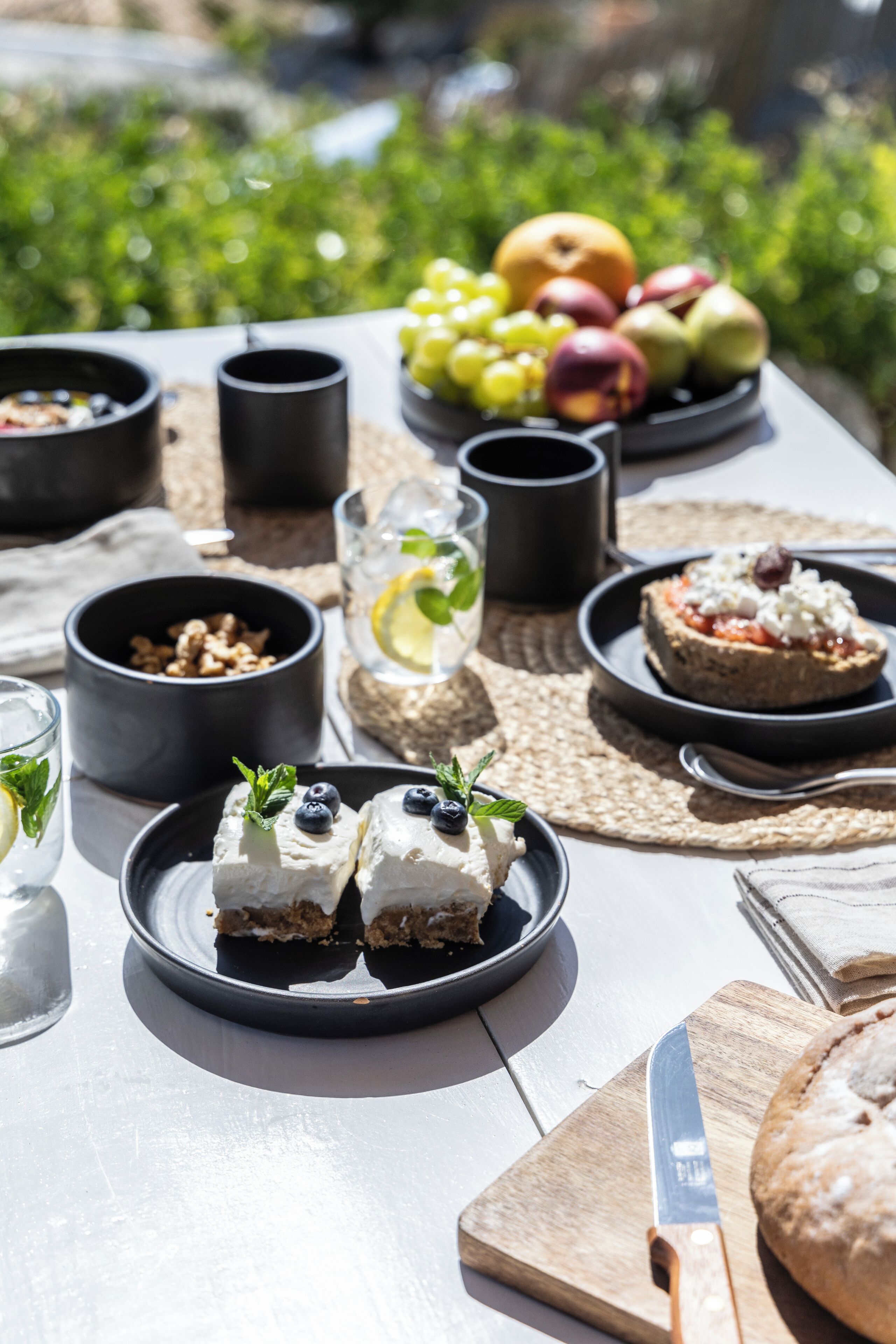 Een picknickopstelling met eten en drinken op een tafel, omringd door groen.