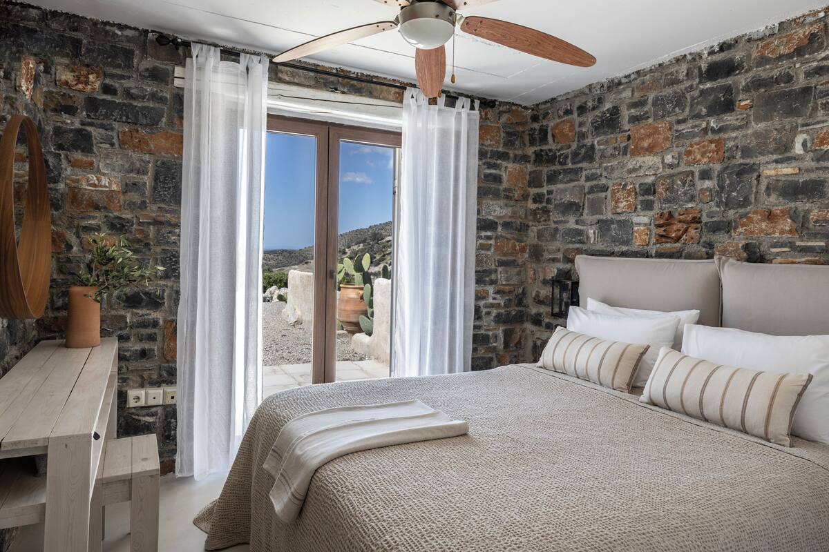 Un dormitorio con pared de piedra, cama de madera, ventilador de techo y vistas al exterior.