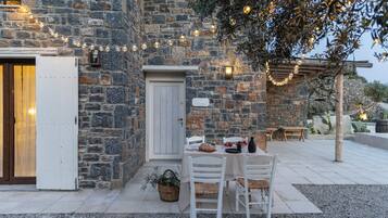 A stone building with a white door, outdoor seating, and string lights.