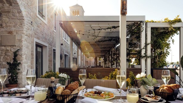 An outdoor dining area with stone walls, wooden tables, and a pergola covered with vines. - Palace Divnic by Armerun Heritage Hotel (Sibenik)