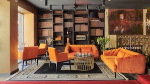 A modern living room with a large orange sofa, matching armchairs, and a coffee table. There is a bookshelf filled with books and a painting on the wall. - Palace Divnic by Armerun Heritage Hotel (Sibenik)