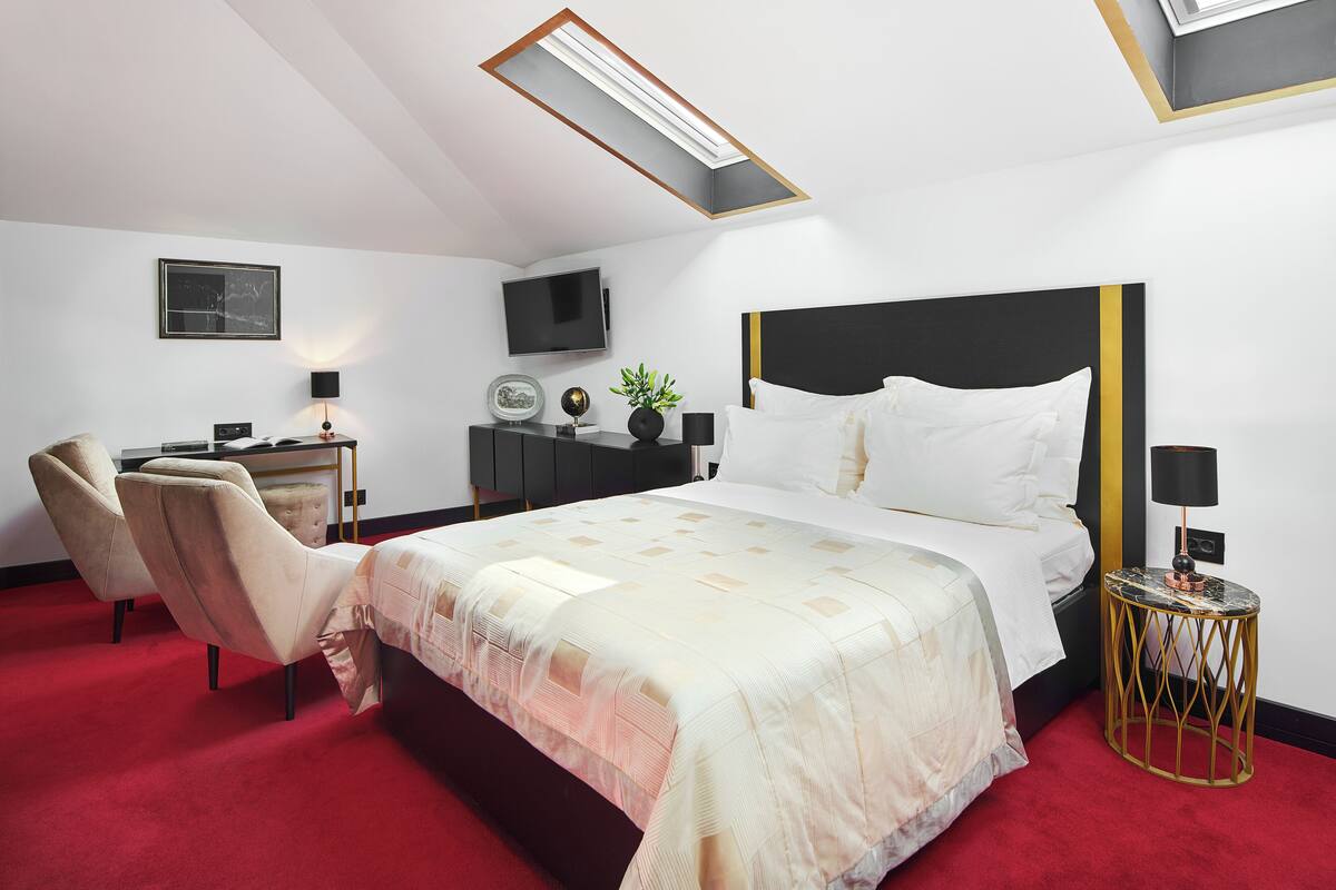 Ein Hotelzimmer mit einem Bett, einem Schreibtisch, einem Stuhl, einem Fernseher und einem kleinen Tisch mit einer Lampe.