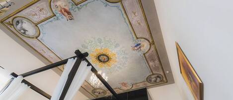 A room with a high ceiling featuring ornate frescoes and a chandelier.
