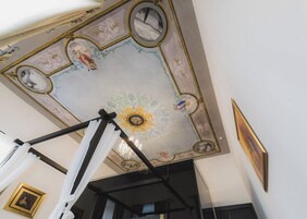 A room with a high ceiling featuring ornate frescoes and a chandelier.
