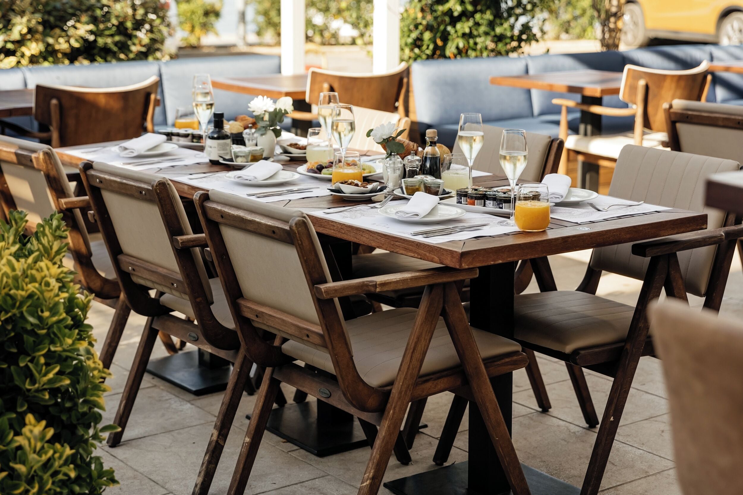 Un espacio de comedor al aire libre con mesas y sillas de madera, una variedad de platos y bebidas, y un sofá azul al fondo.