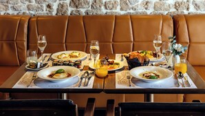 A dining table set with plates of food, glasses of water and wine, and a vase with flowers. - Palace Divnic by Armerun Heritage Hotel (Sibenik)