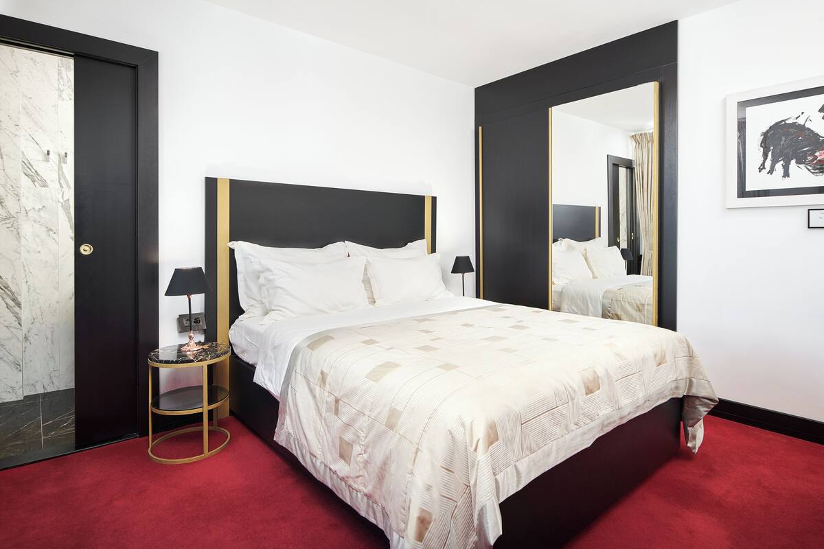 Ein Hotelzimmer mit einem großen Bett, einem runden Beistelltisch, einem Spiegel und einem gerahmten Bild an der Wand.