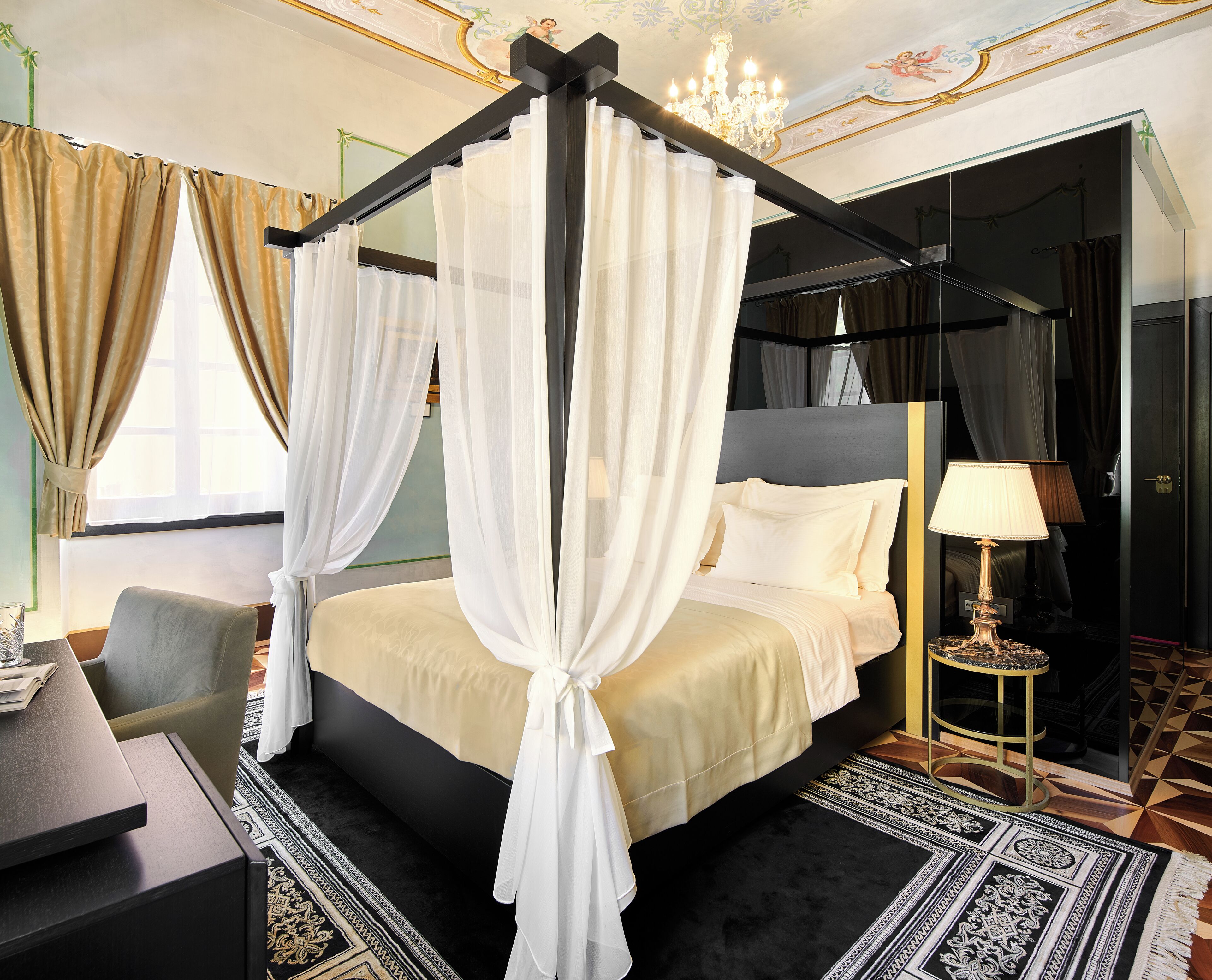 A luxurious bedroom with a canopy bed, a bedside table, a chair, and a nightstand with a lamp.