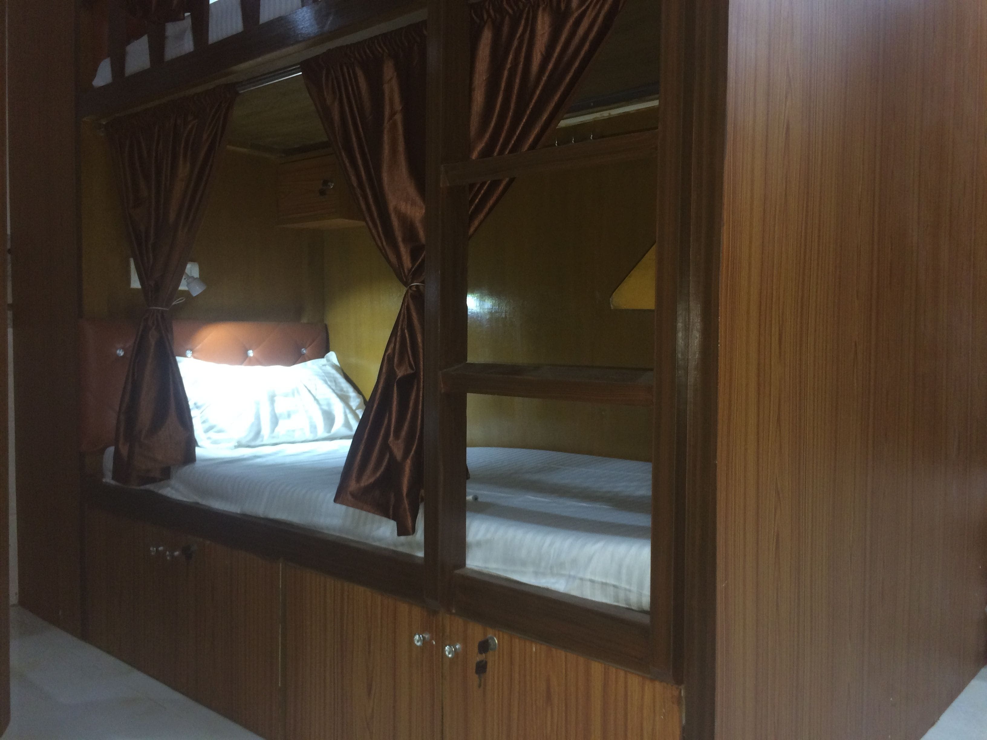 Ein Stockbett mit Vorhängen, Holzwänden und einer Bettauslage mit Kissen.