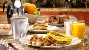 Una escena de desayuno con una cafetera, un bol de fruta, tortitas, una tortilla y zumo de naranja.