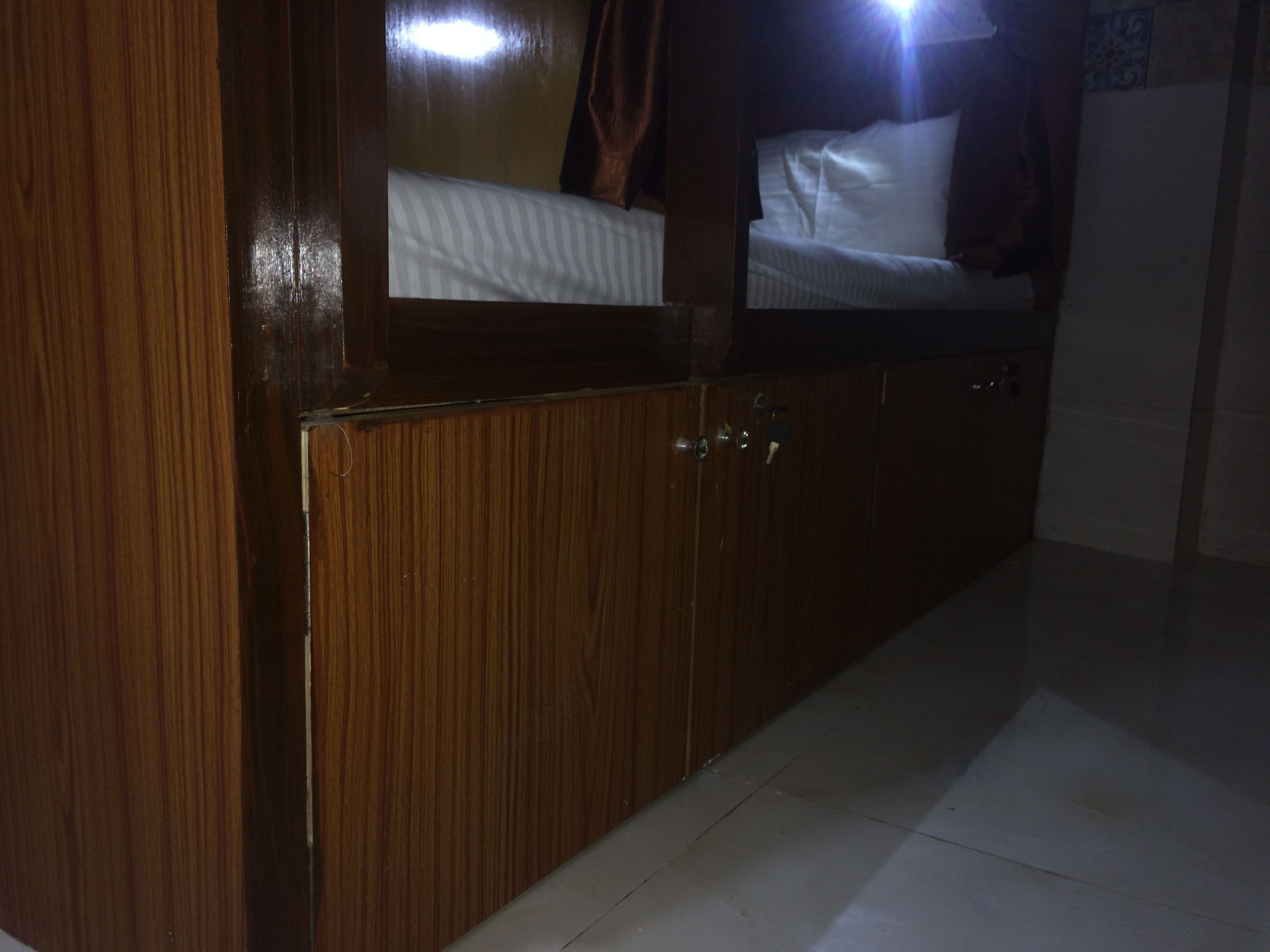 Un armario de madera con espejo, una cama con ropa de cama blanca y un suelo de baldosas.