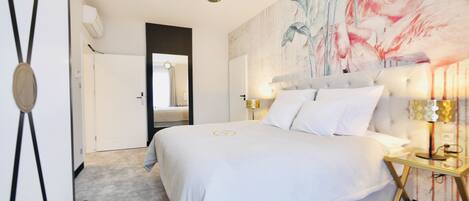 A modern hotel room with a large bed, a headboard with a floral mural, bedside lamps, and a view of the hallway.