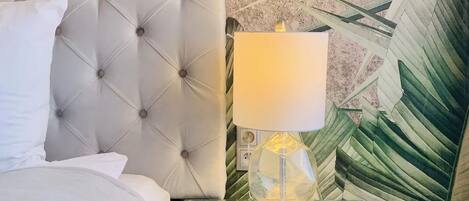 A bed with a tufted headboard, a bedside table with a glass top, and a lamp with a clear glass shade.