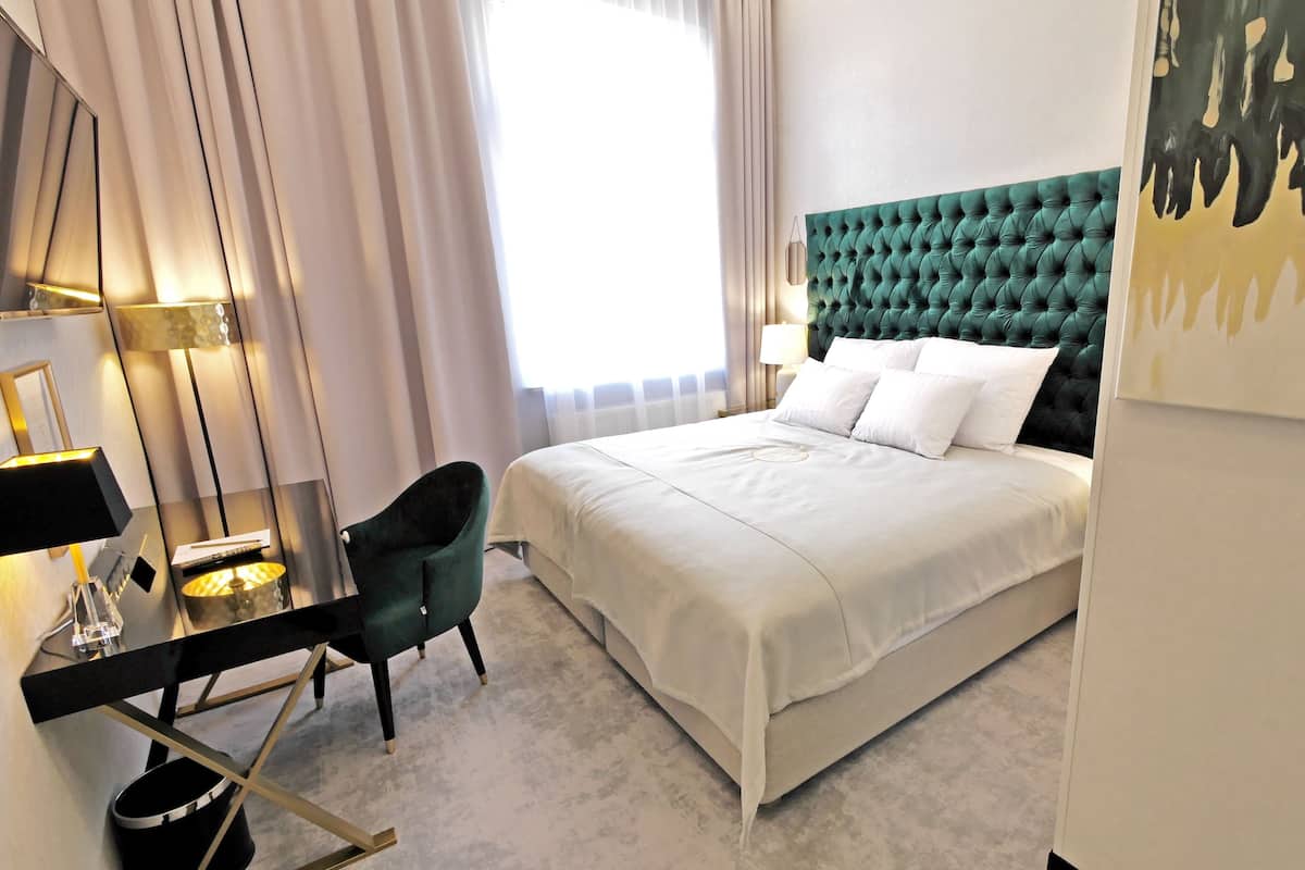 Una habitación de hotel moderna con una cama grande, un escritorio con silla, una lámpara y un cuadro en la pared.