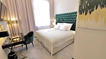 A modern hotel room with a large bed, a desk with a chair, a lamp, and a painting on the wall.