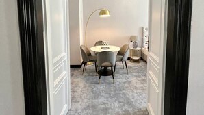 Un couloir mène à une salle à manger où se trouvent une table ronde, des chaises et une lampe.