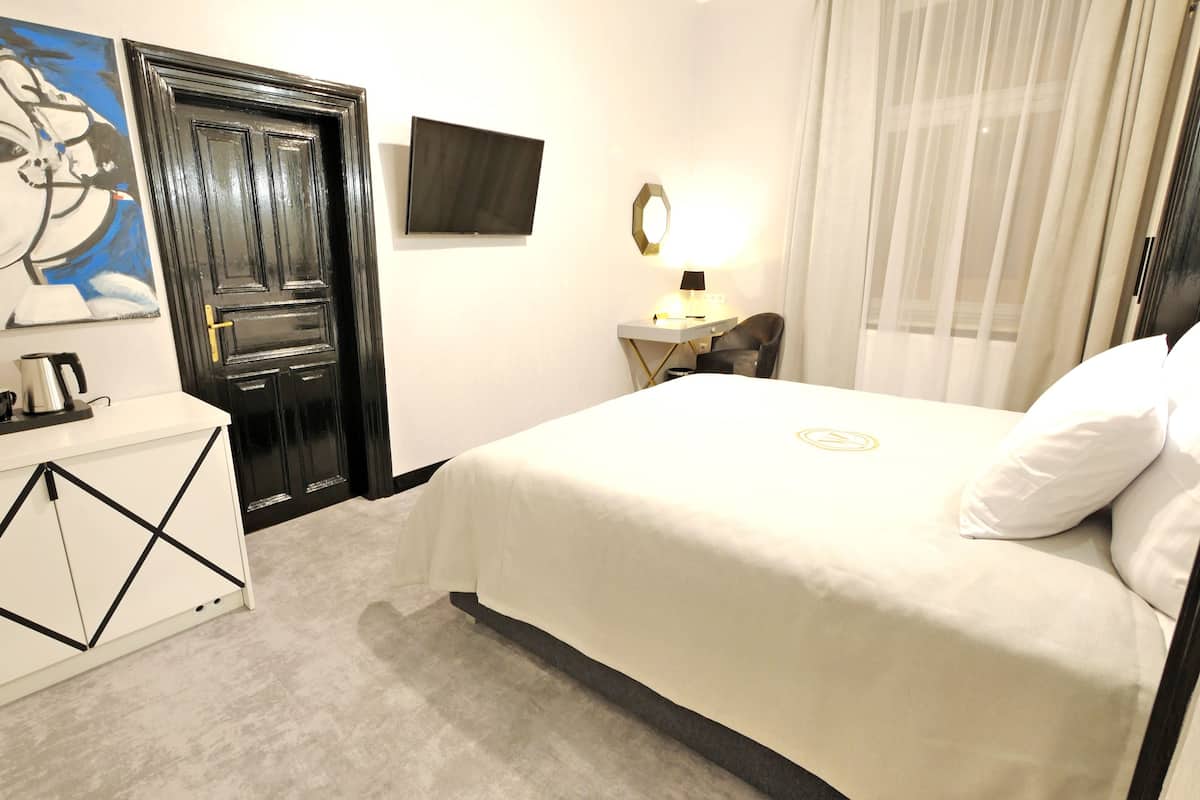 Una habitación de hotel con cama, un escritorio con lámpara, un cuadro y una puerta.
