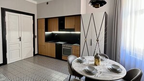 Un espace repas moderne avec une table ronde dressée pour quatre personnes, une cuisine en arrière-plan et une grande fenêtre avec des rideaux.