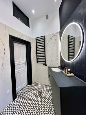 Een moderne badkamer met een witte deur, een zwarte handdoekhouder en een ronde spiegel met verlichting.