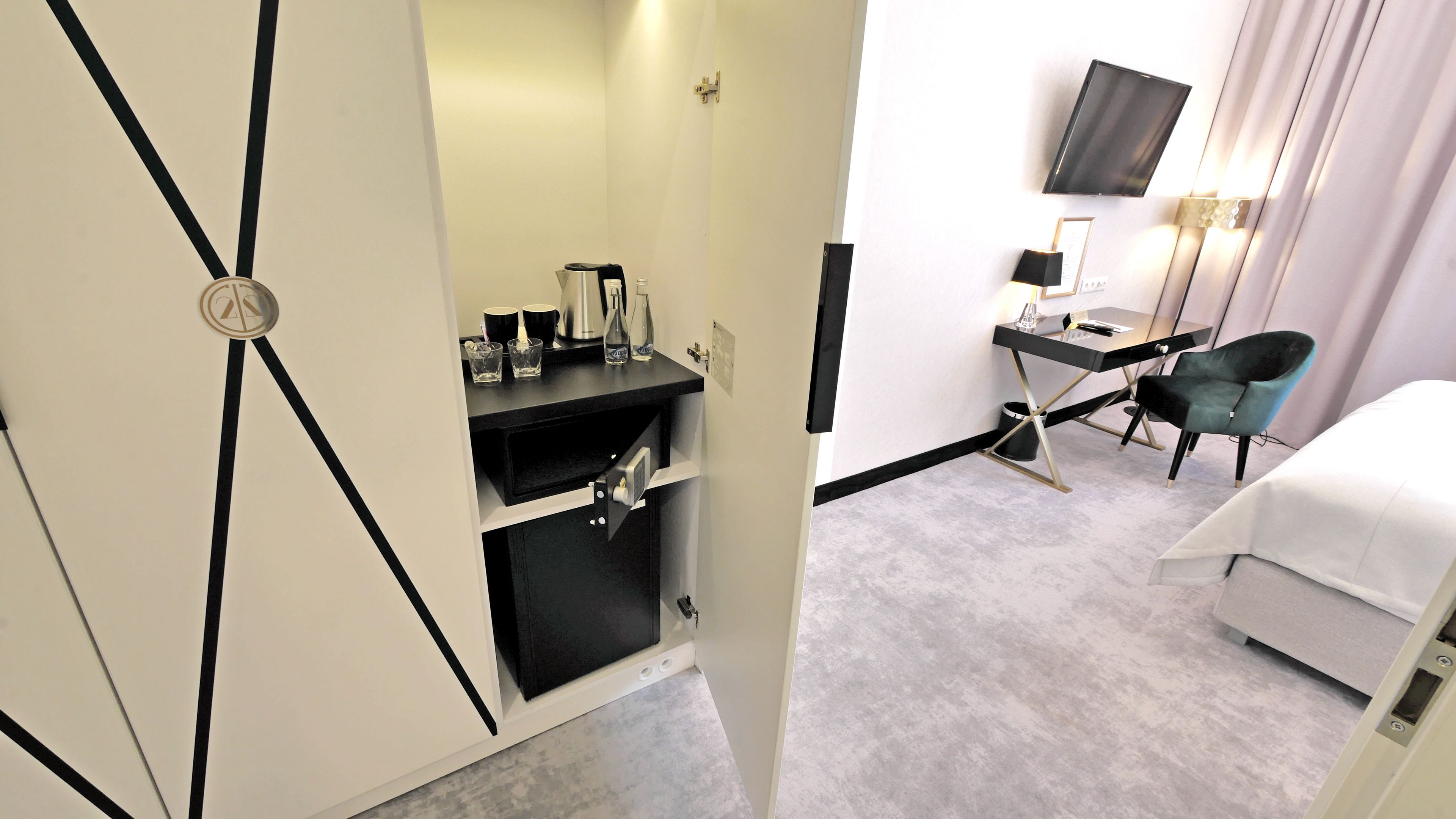 Ein Hotelzimmer mit einem Bett, einem Schreibtisch mit Stuhl, einem Fernseher und einer Minibar.