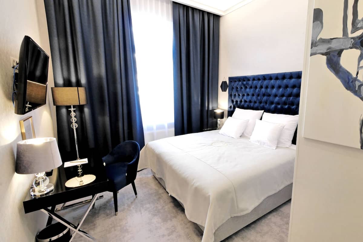 Habitación de hotel con una cama grande, un escritorio con una silla, una lámpara y un cuadro en la pared.