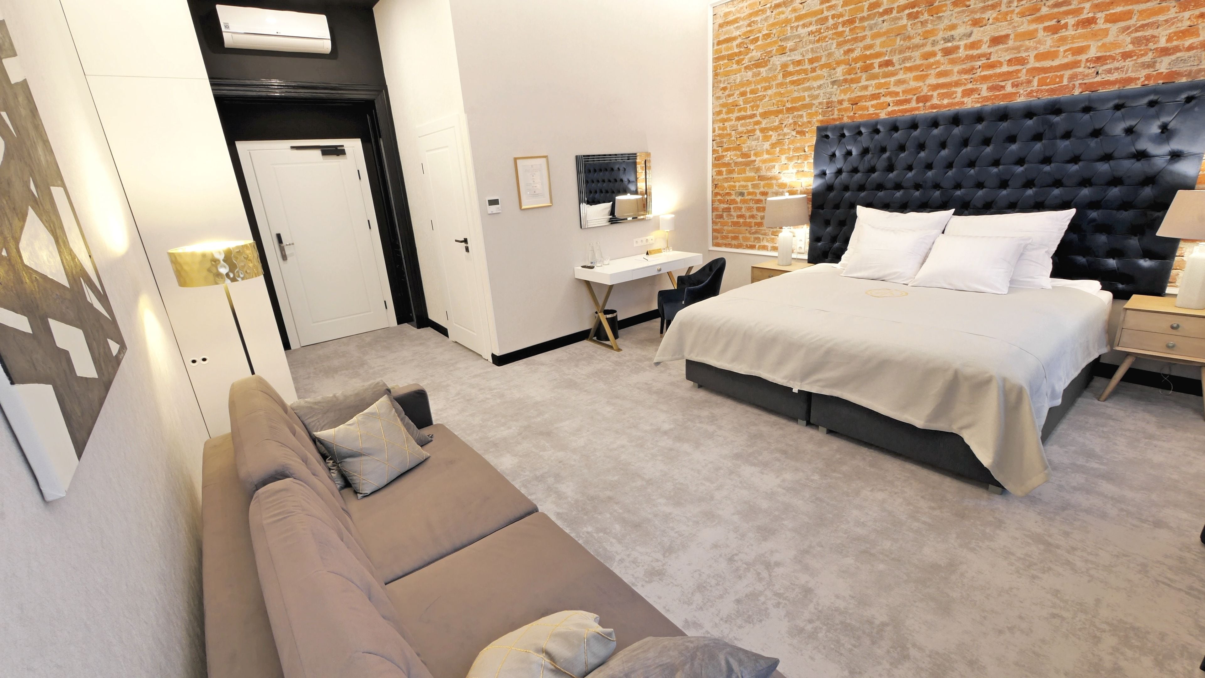 A hotel room with a large bed, a sitting area with a sofa, a desk, and a brick wall.