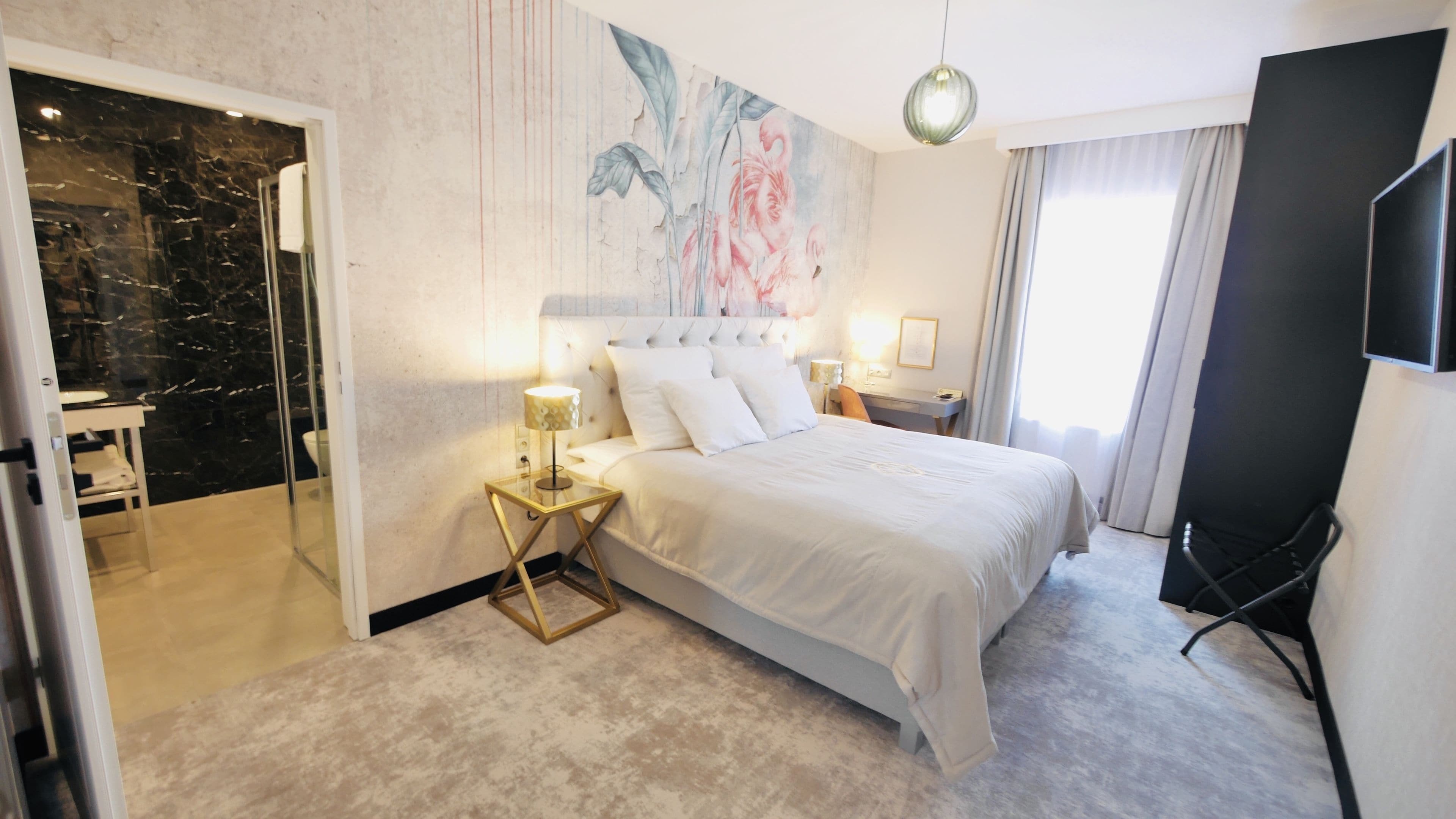 A hotel room with a bed, a desk, a chair, a TV, and a bathroom with a glass door.