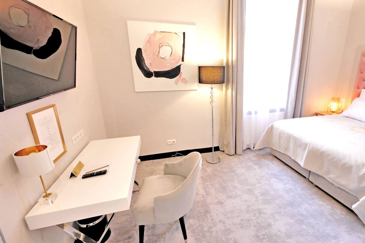 Habitación de hotel con una cama, un escritorio, una silla, una lámpara de pie y obras de arte en las paredes.