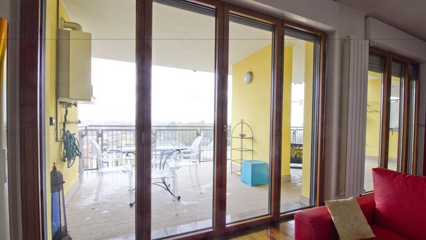 Une pièce avec un canapé rouge, une porte-fenêtre coulissante donnant sur un balcon extérieur équipé de chaises et d’une table.