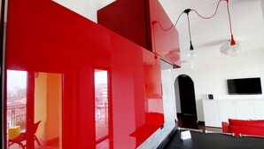 Un salon moderne aux couleurs rouge et blanche, doté d’un téléviseur à écran plat et offrant une vue sur la ville grâce à de grandes fenêtres.