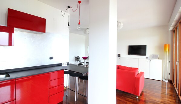 A modern kitchen with red cabinets and a dining area with a red sofa.