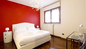 Een slaapkamer met een wit bed, rode muren, een houten vloer, een glazen tafel en een raam met gordijnen.