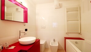 Een moderne badkamer met een wit wastafel, een rode wastafelmeubel, een wit toilet, een wit bidet en een witte badkuip.