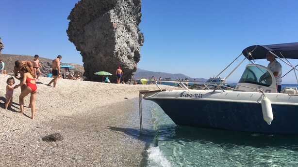 A beach with clear water, a rocky formation, and a boat. - Hostal La Isla (Carboneras)