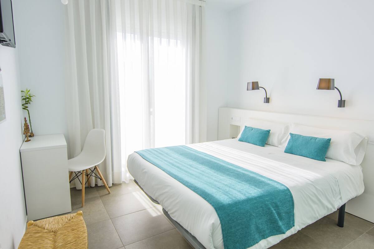 A hotel room with a bed, a desk, a chair, and a window with curtains.